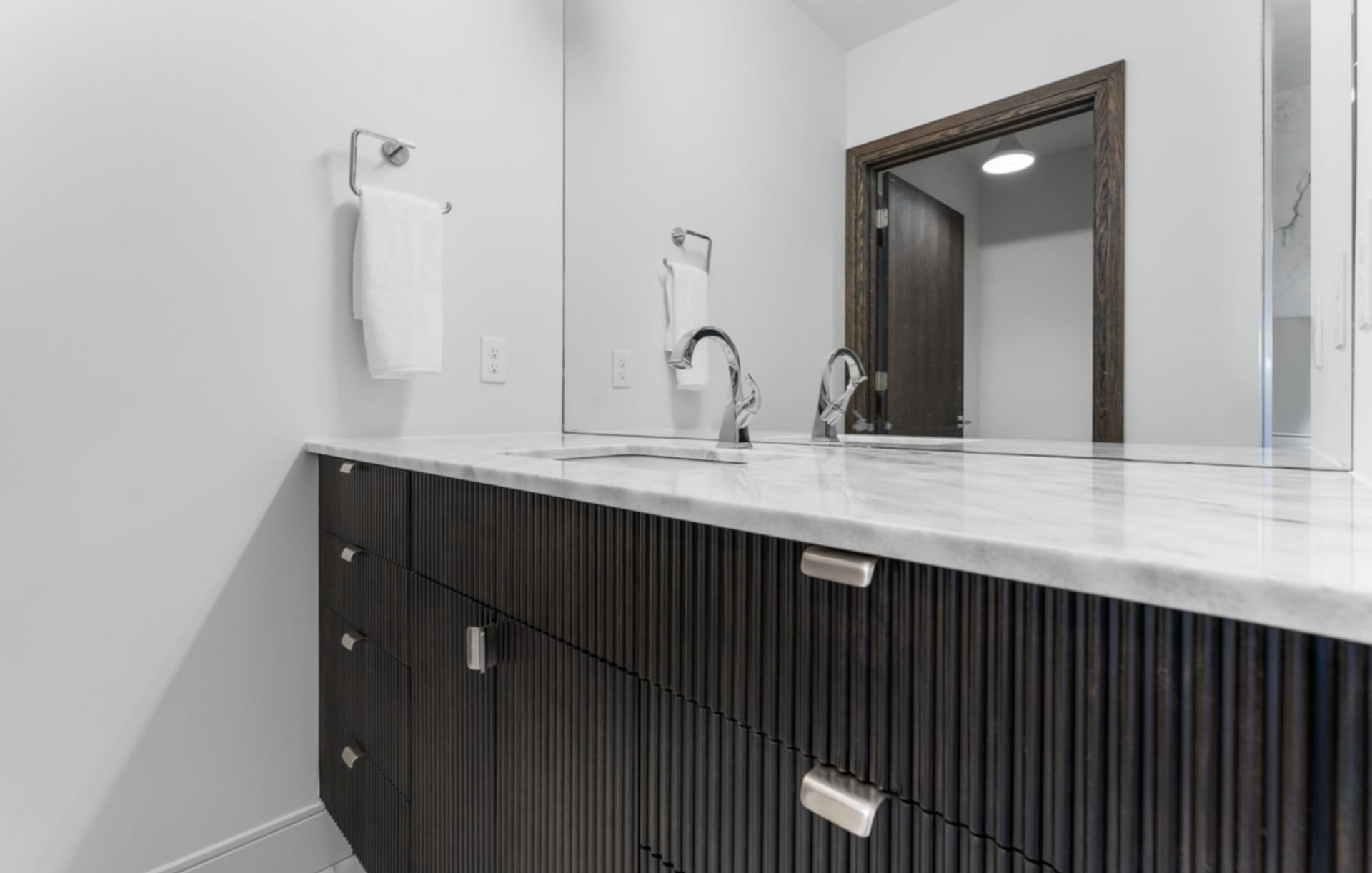 Modern bathroom with dark wood vanity, marble countertop, and chrome fixtures.