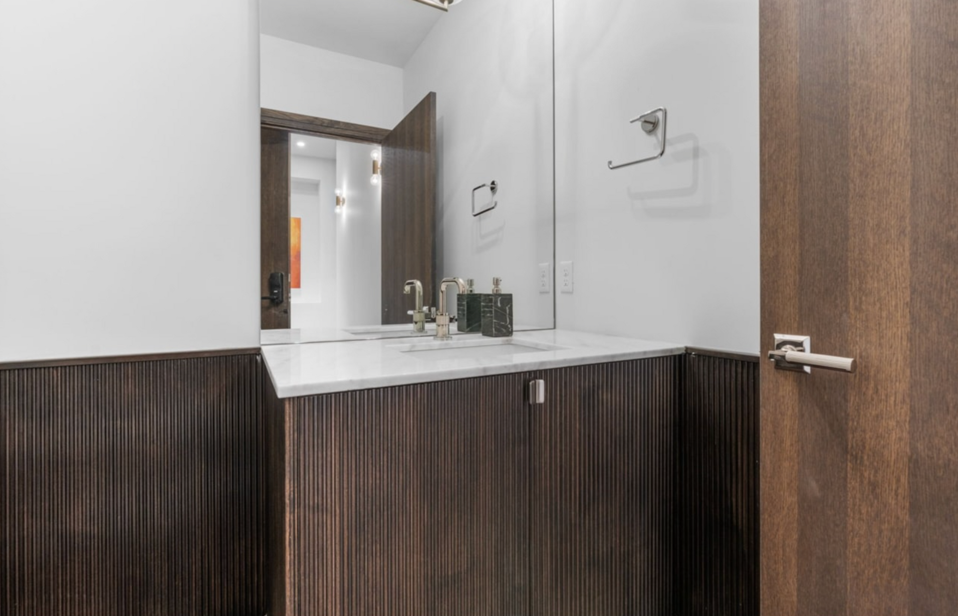 Dark wood powder room with white countertop, silver fixtures, and large mirror.