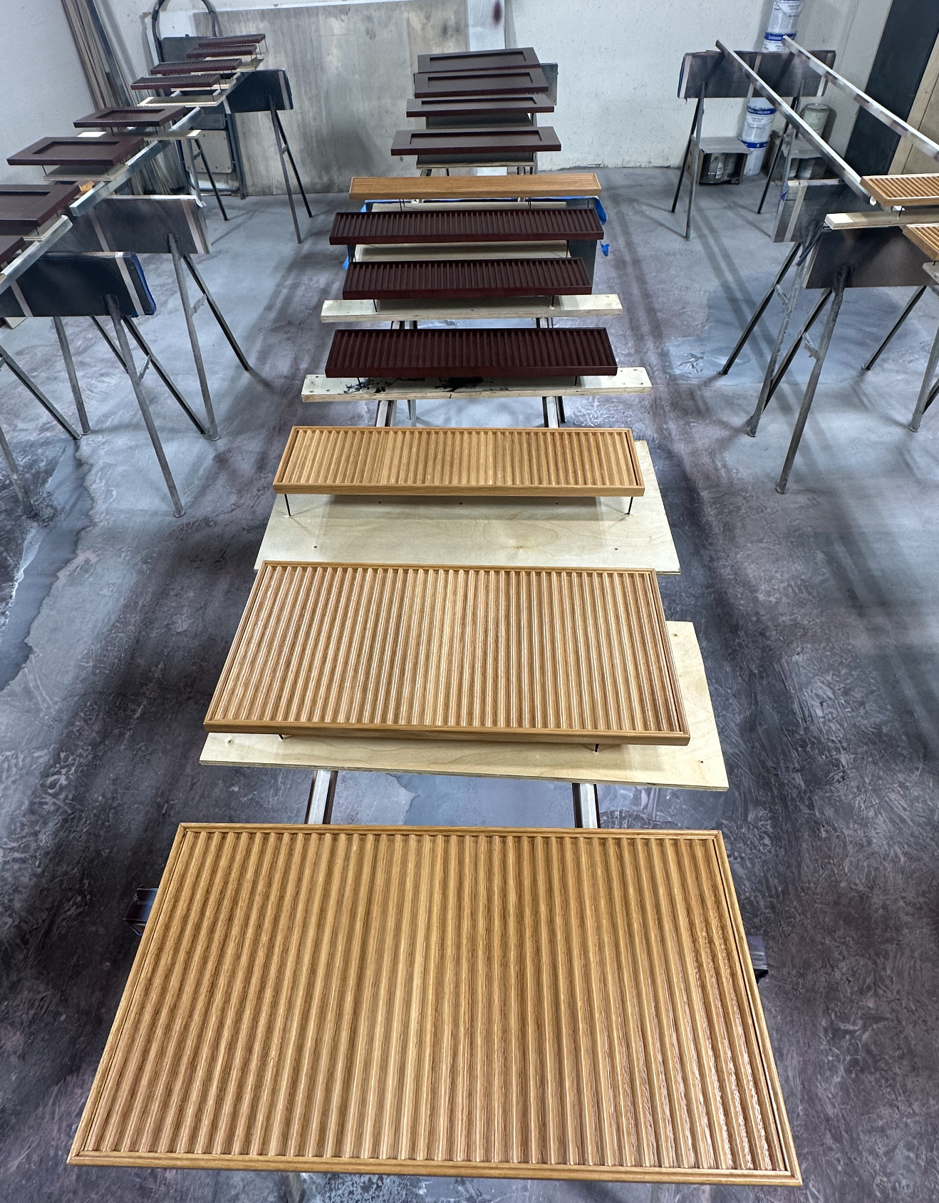 Wooden panels in various shades and textures, arranged on work stands in a workshop setting.