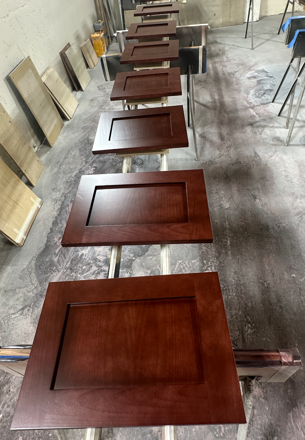 Cabinet doors, stained a rich brown, drying on racks in a workshop.