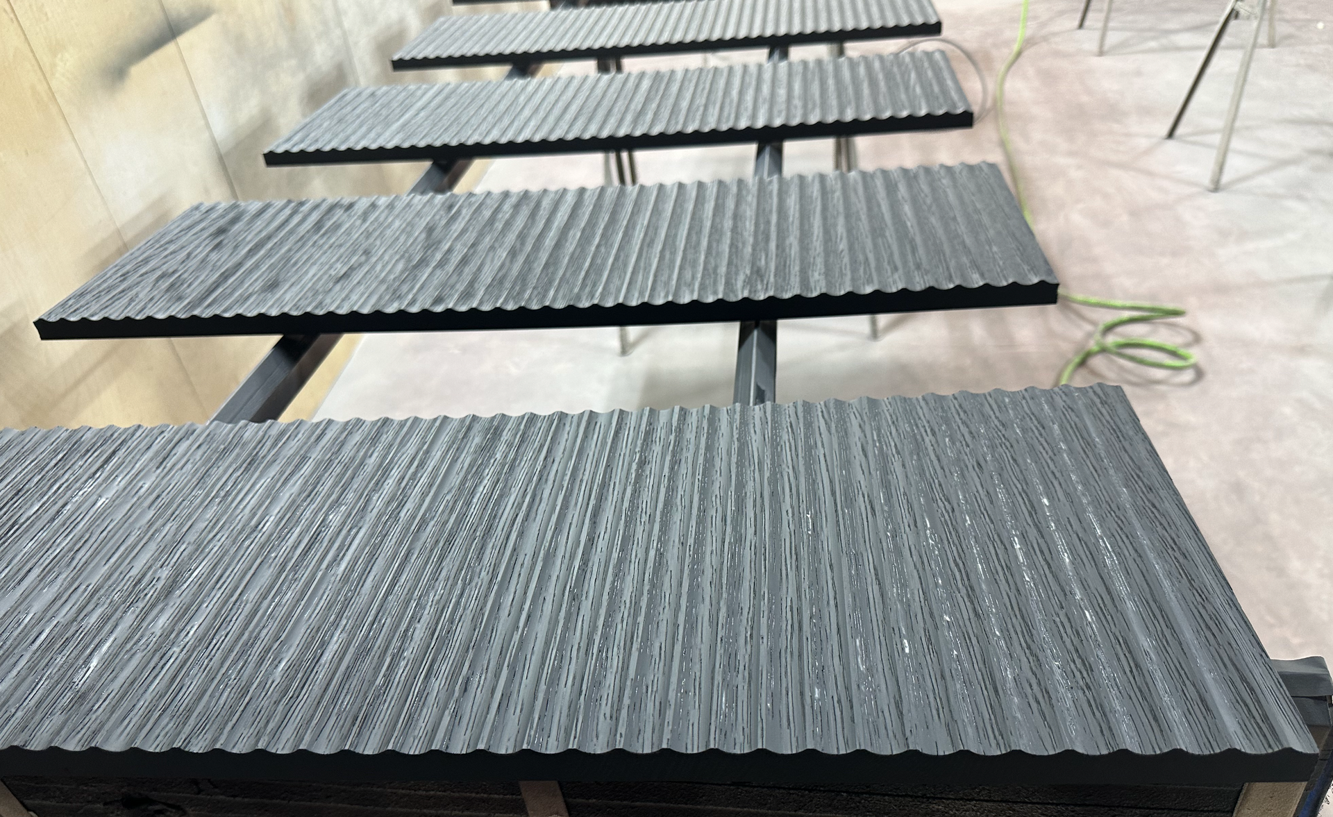 Rows of textured, dark gray panels on black supports, likely being painted in a workshop.