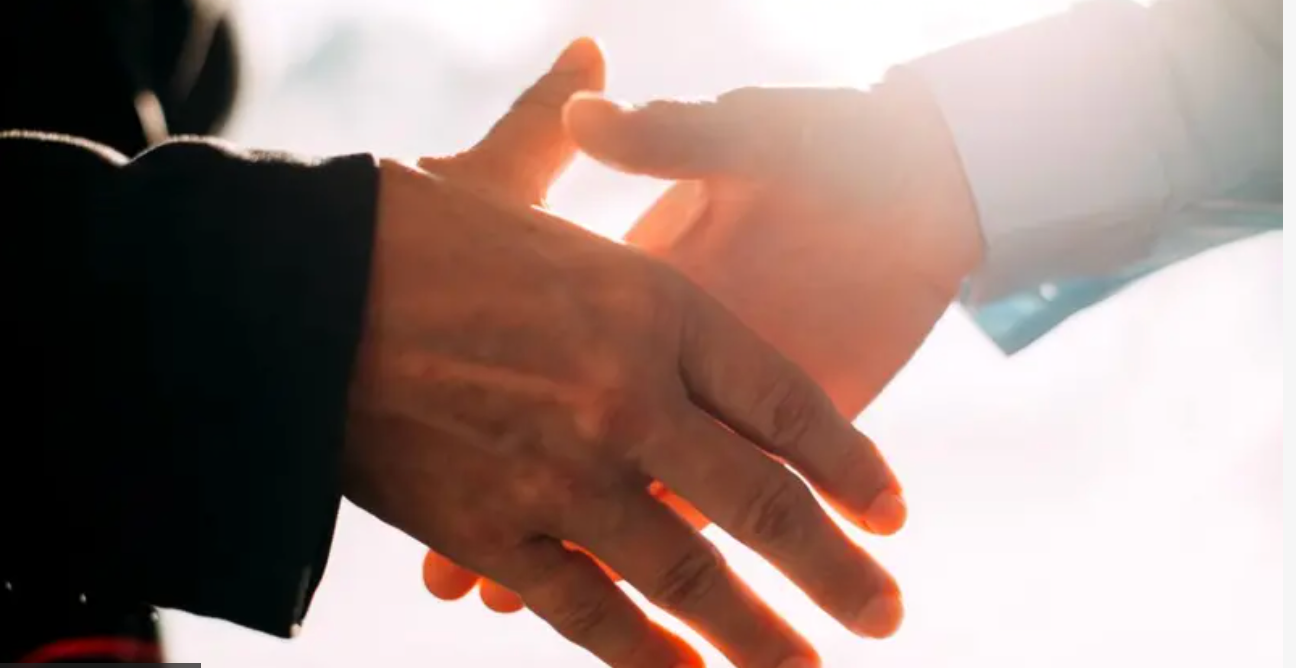 Two people shaking hands, symbolizing agreement, collaboration, or a deal. Backlit with bright light.