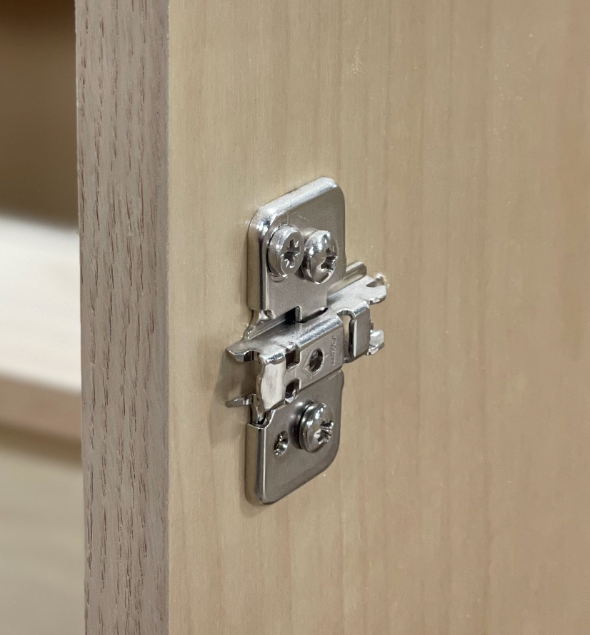 Silver cabinet hinge mounted on light wood.