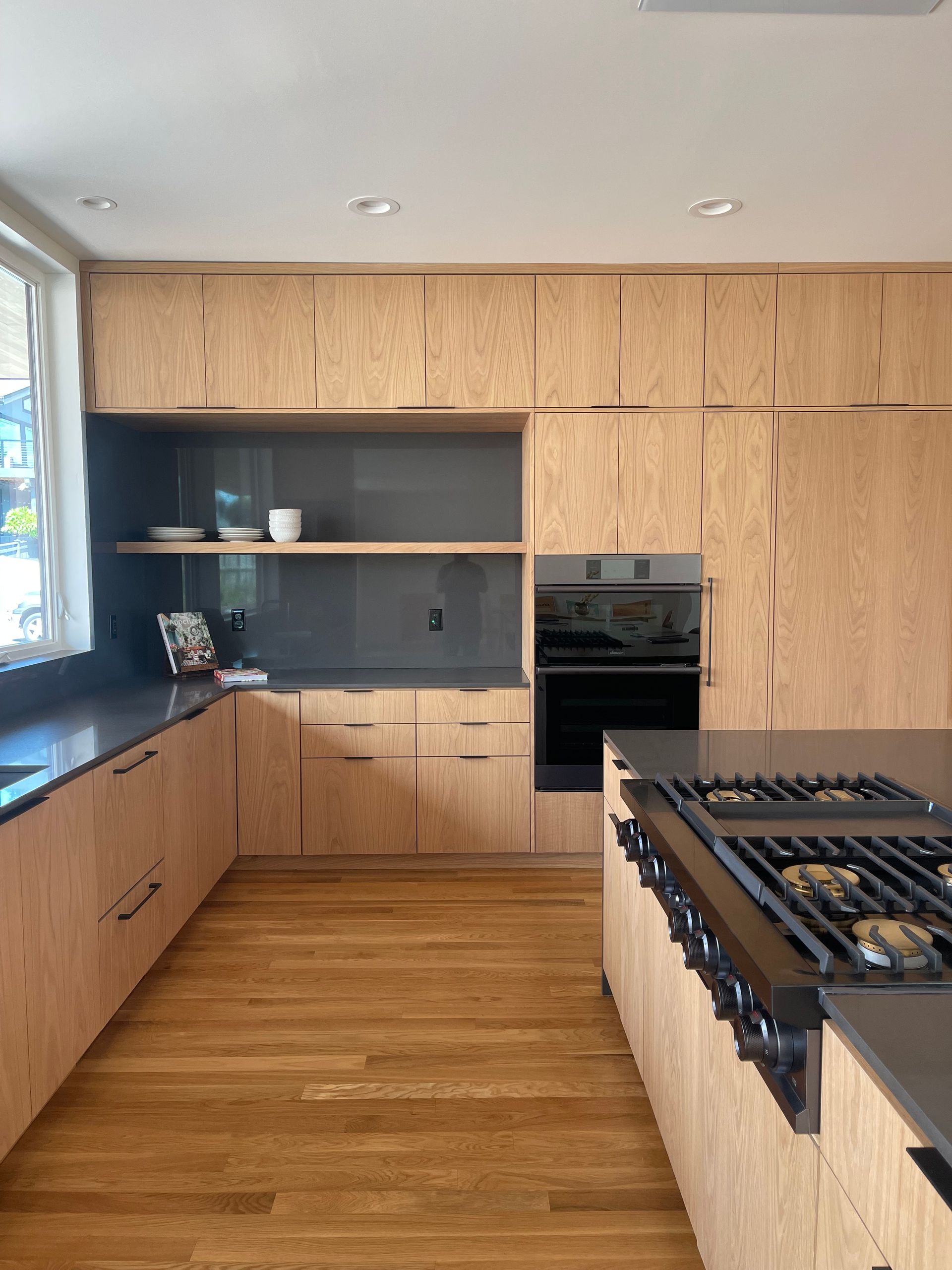 Modern kitchen with light wood cabinets, dark countertops, and stainless steel appliances.