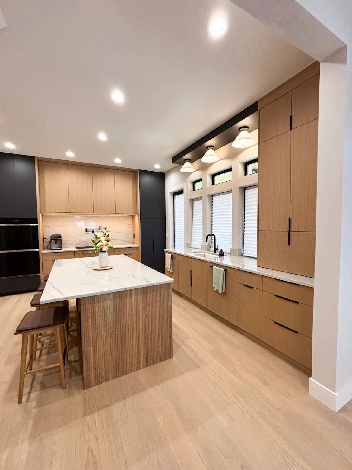 Modern kitchen with light wood cabinets, white countertops, and a marble island.