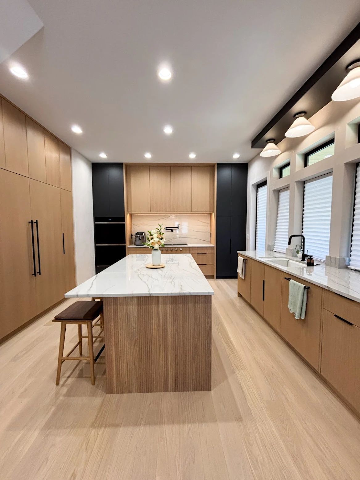 Modern kitchen with light wood cabinets, white countertops, black accents, and large island.