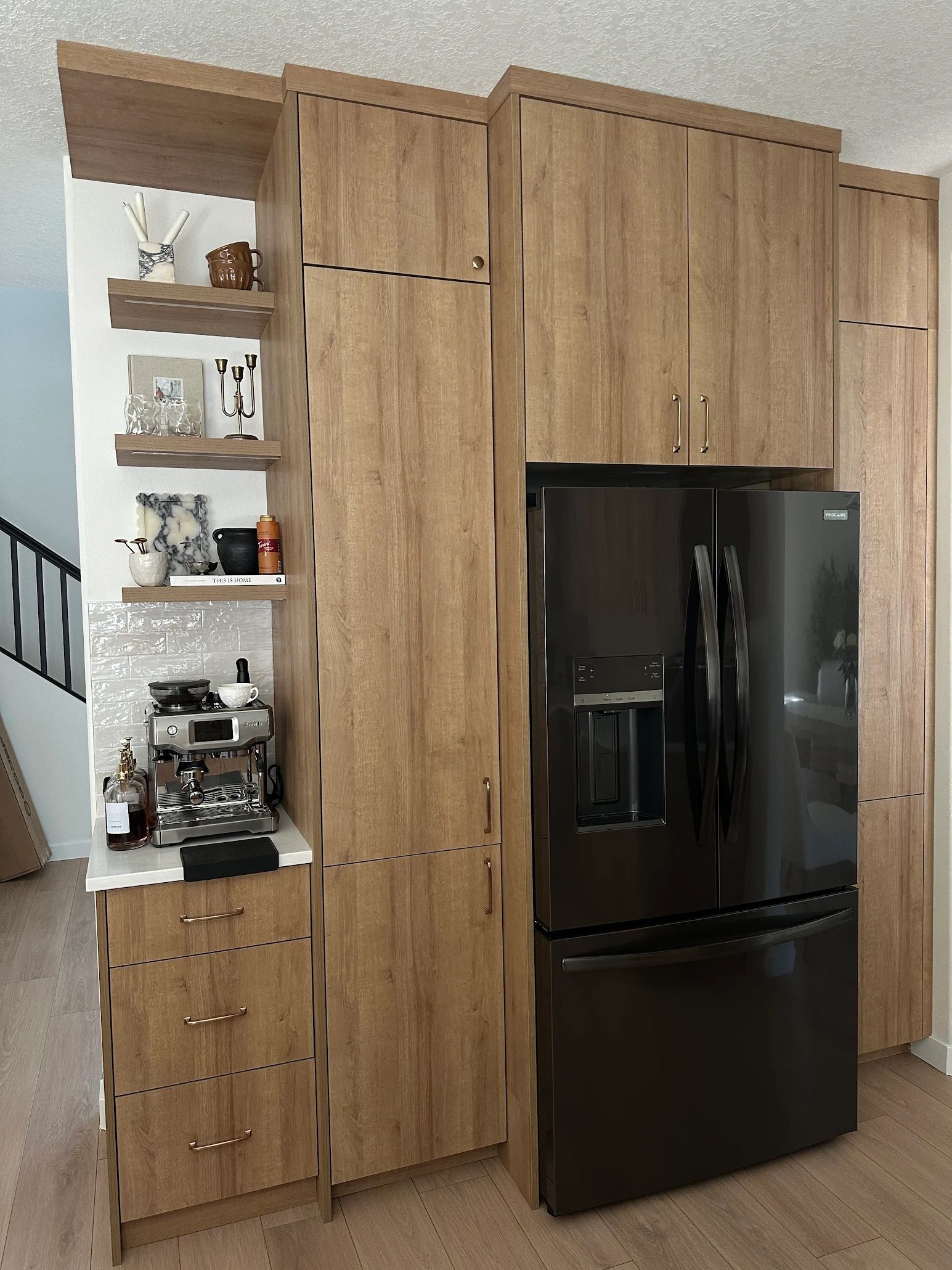 Tall wooden cabinets and refrigerator in a kitchen. Open shelves on the left, black fridge on the right.