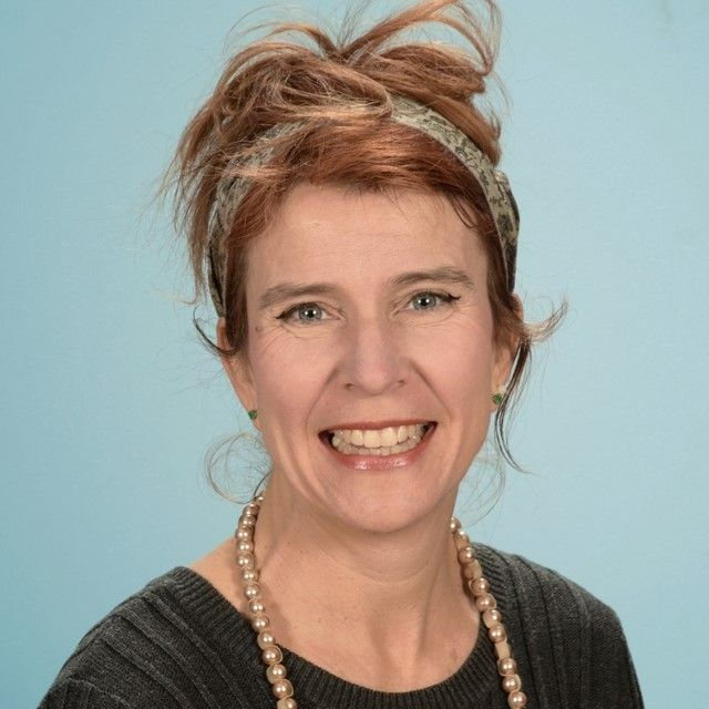 A woman wearing a black shirt and a necklace is smiling for the camera.