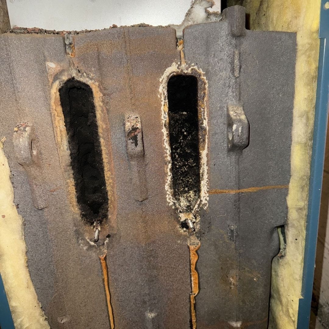 Exterior view of an old furnace door showing two large, dark, rectangular openings and rust.