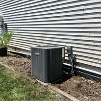 Furnace in a basement; gray metal unit, ductwork, brick walls.