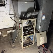 Blue furnace and green expansion tank in a basement with water heater, exhaust pipes.