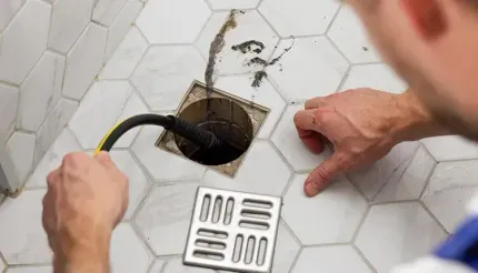 Person unclogging shower drain with a drain snake tool.
