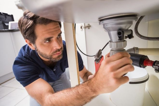 Man working on plumbing under a sink, using a wrench.