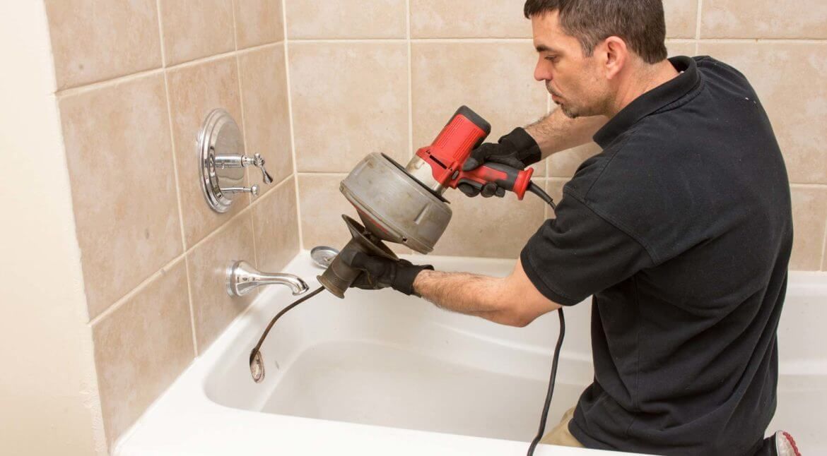 Plumber using a drain snake on a bathtub in a bathroom.