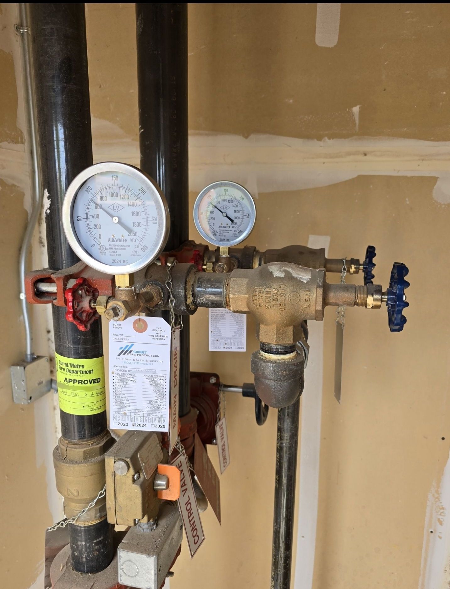 Plumbing system with gauges and valves, likely for fire suppression, against a beige wall.