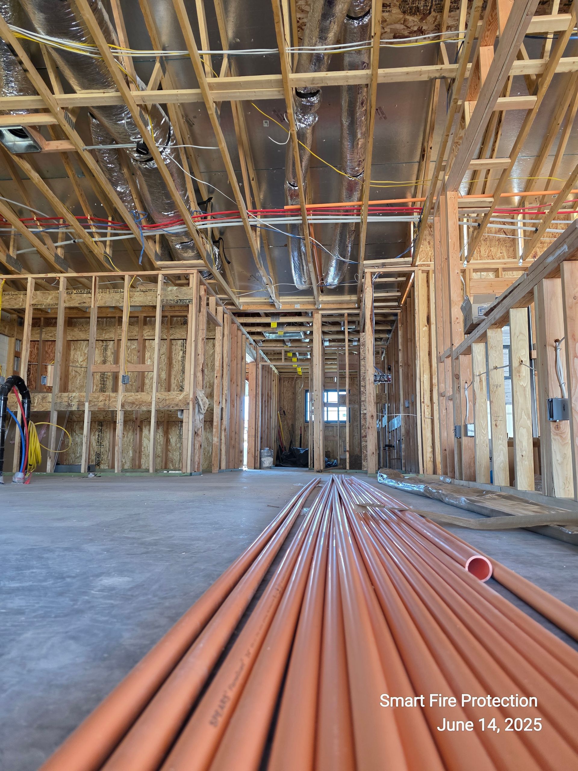 Interior view of a building under construction, with exposed wood framing and orange pipes on the floor.