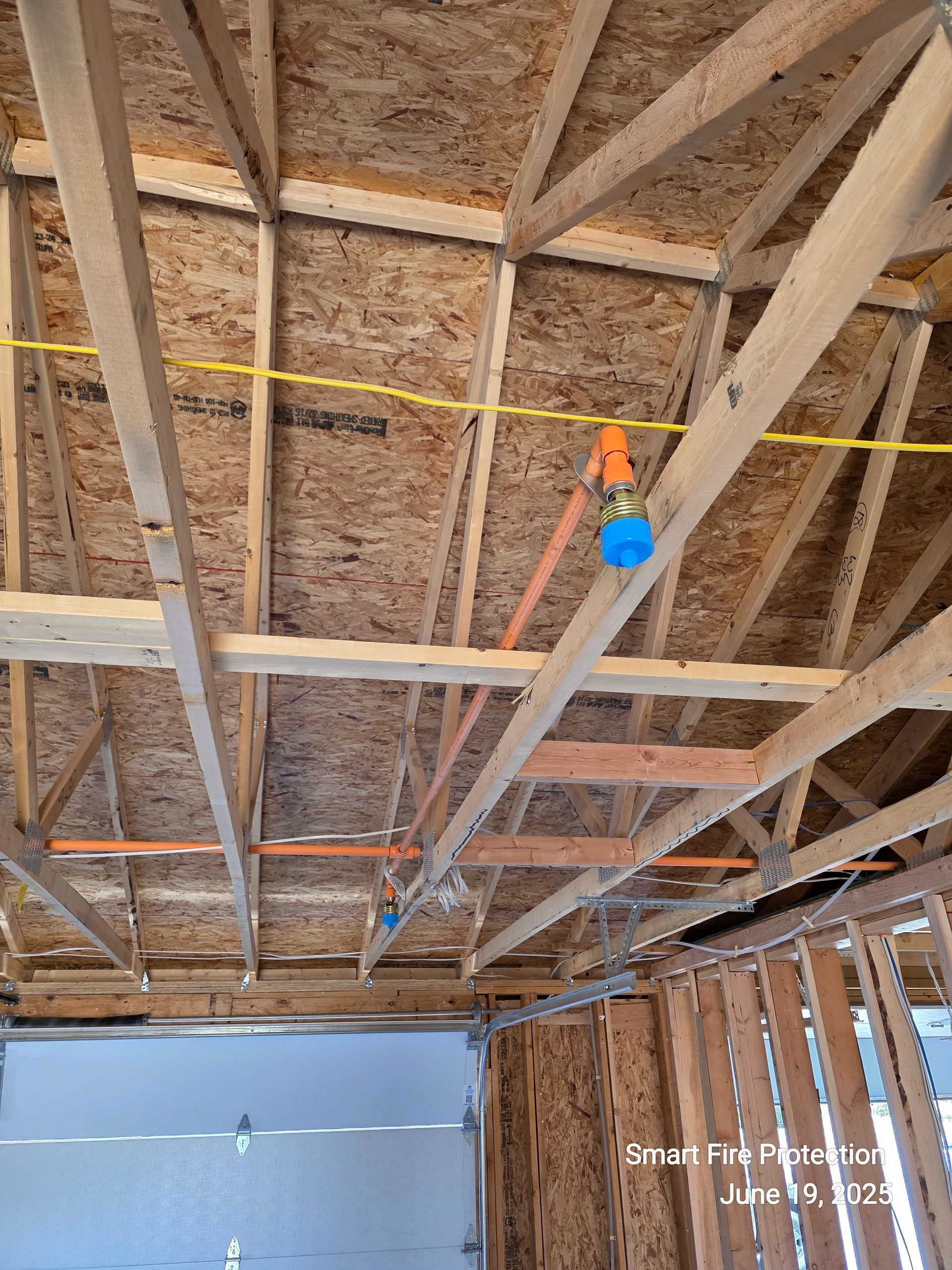 Interior view of unfinished garage ceiling showing wooden trusses, electrical wiring, and light fixtures.
