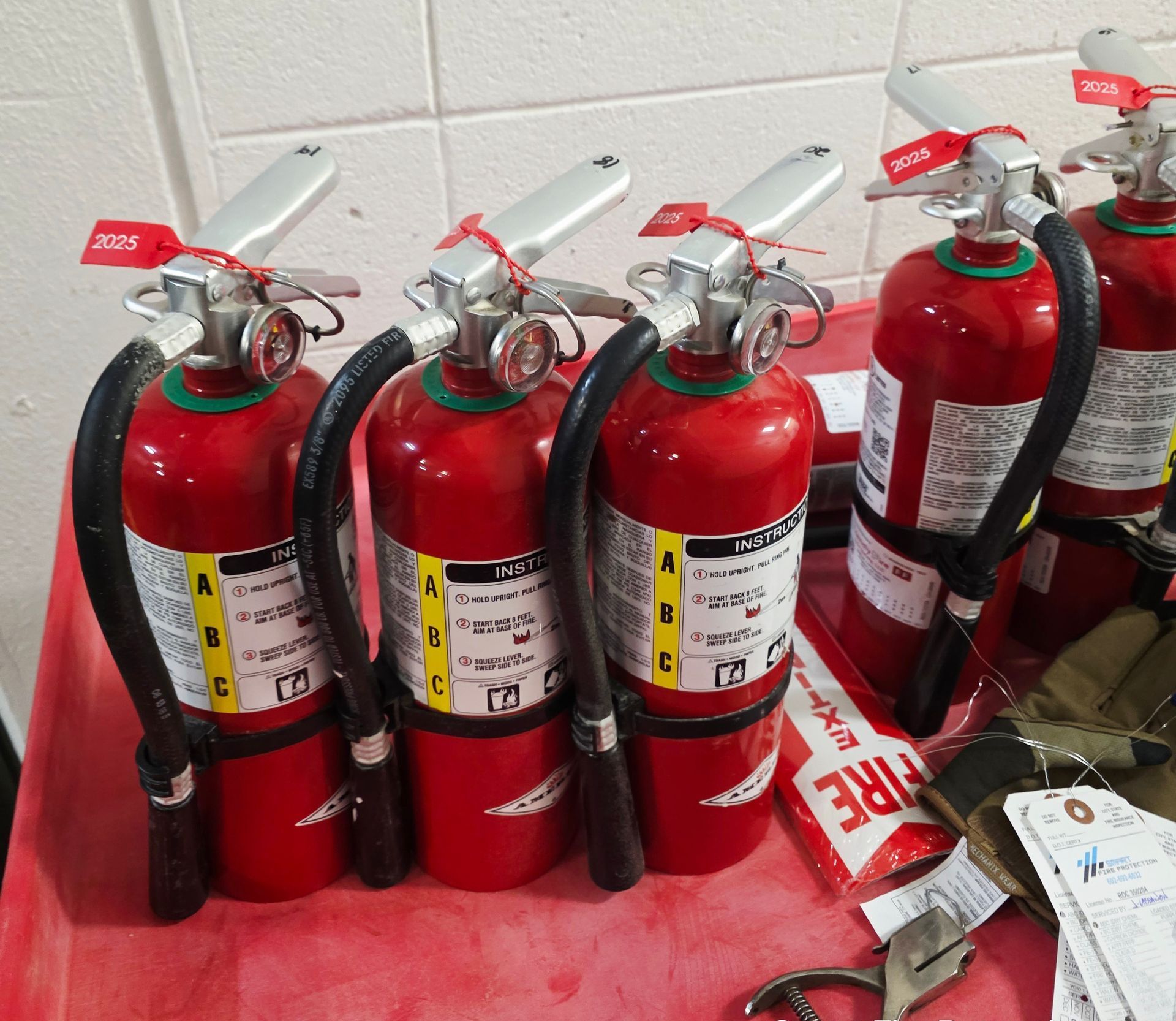 Red fire extinguishers with black hoses and silver handles lined up on a red cart.