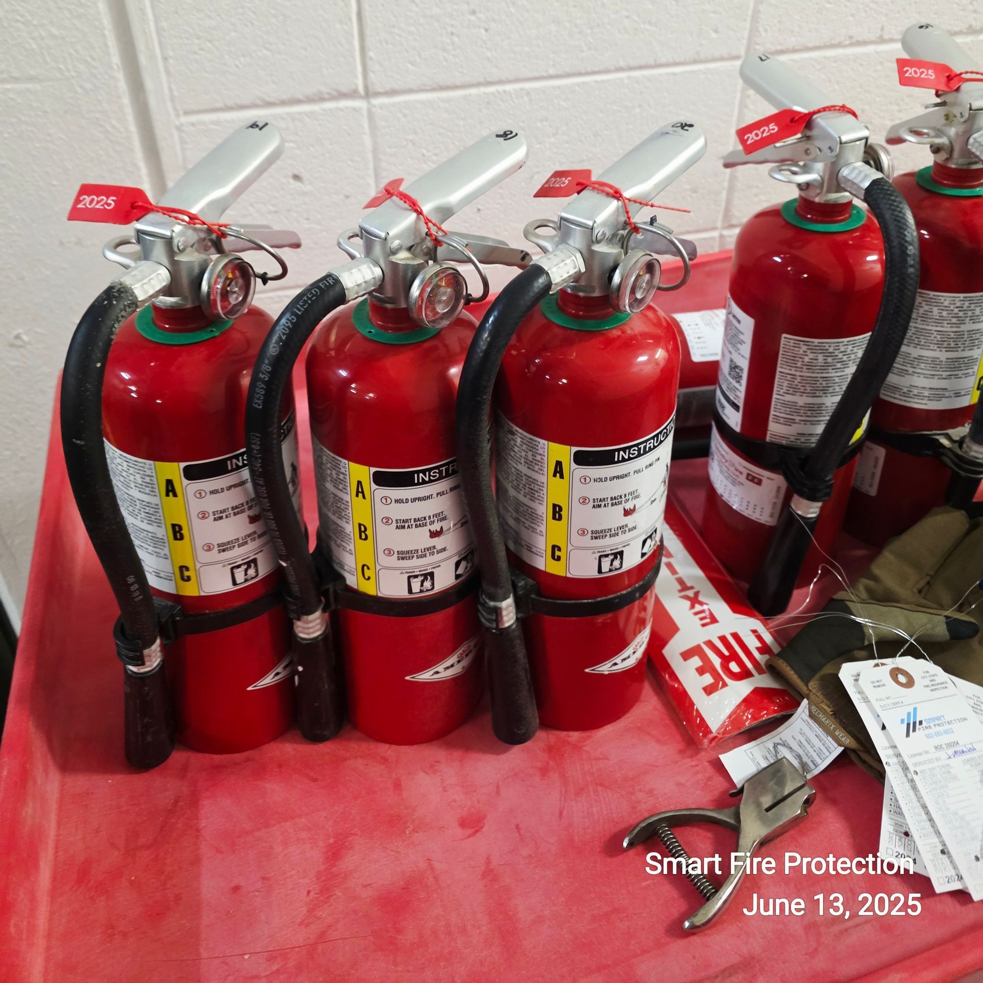 Several red fire extinguishers on a table; tags attached.