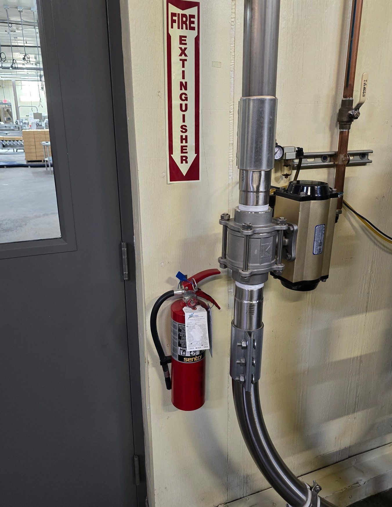 Fire extinguisher next to a metal pipe and valve on a wall with a 