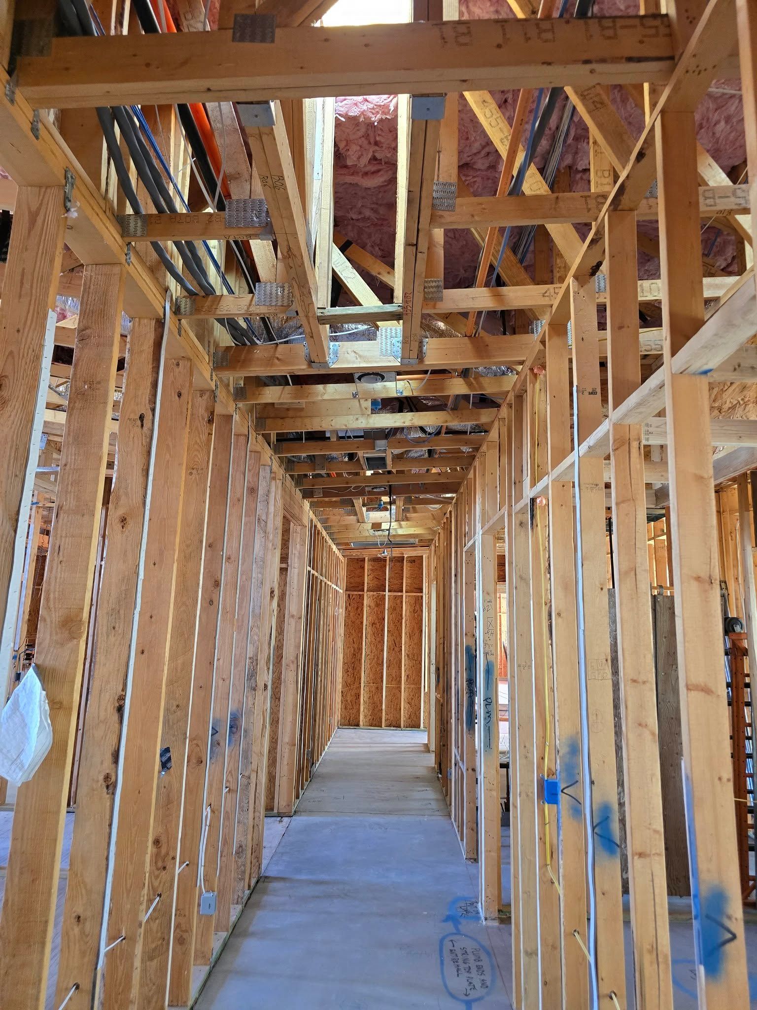Interior framing of a hallway under construction, with exposed wood beams, studs, and wiring.