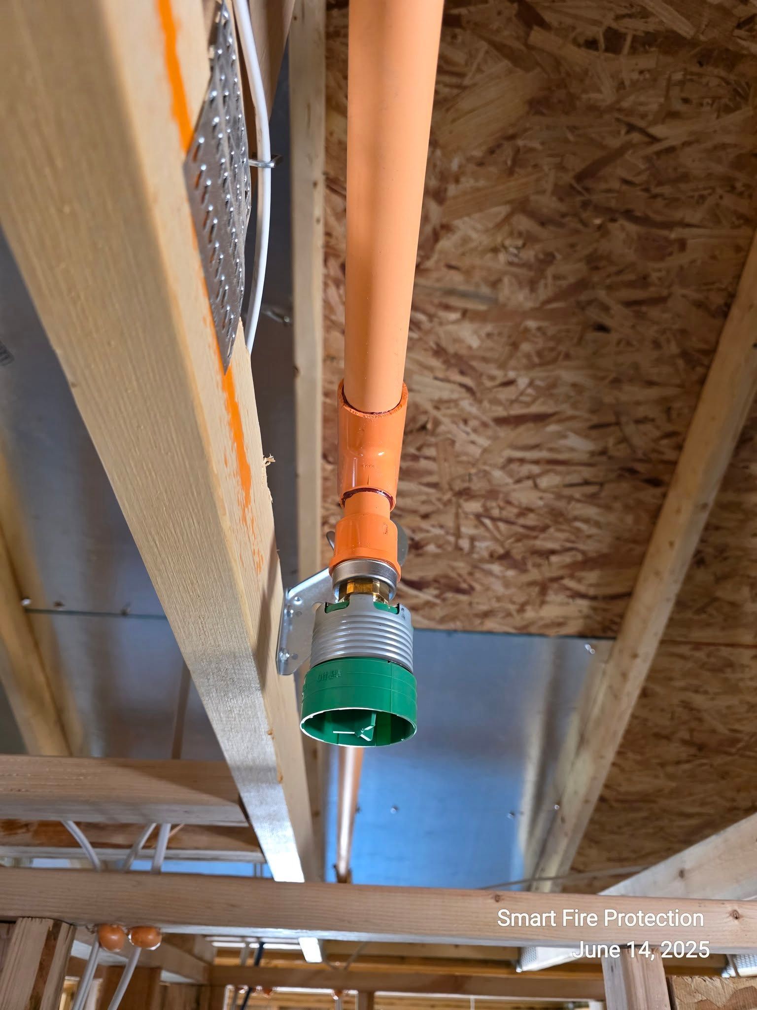 Fire sprinkler head installed in a wooden ceiling. Orange pipe and green/silver sprinkler head.