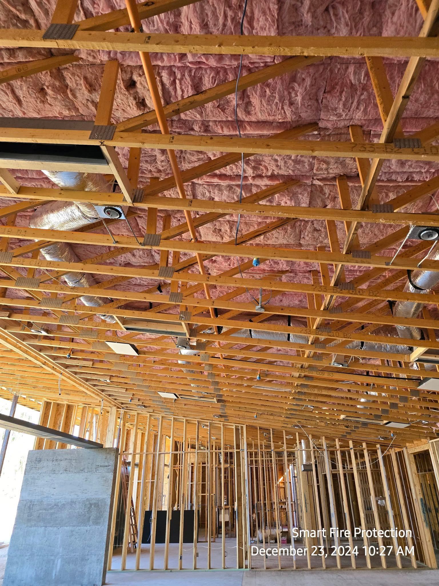Wooden framework of a building under construction, with pink insulation visible in the ceiling.