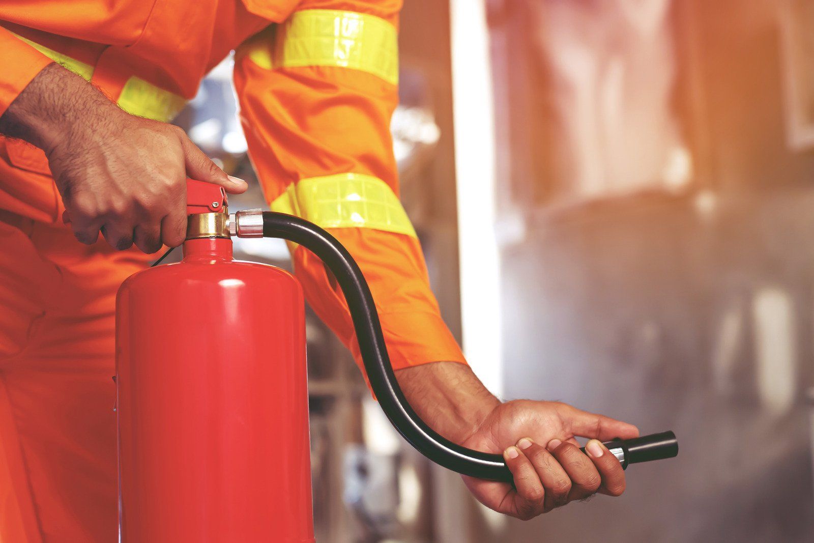 Person in orange uniform operating a red fire extinguisher.