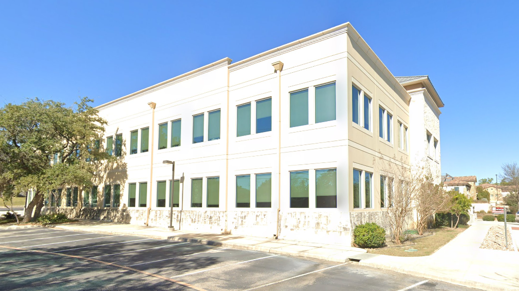 A large white building with a lot of windows and a parking lot in front of it.
