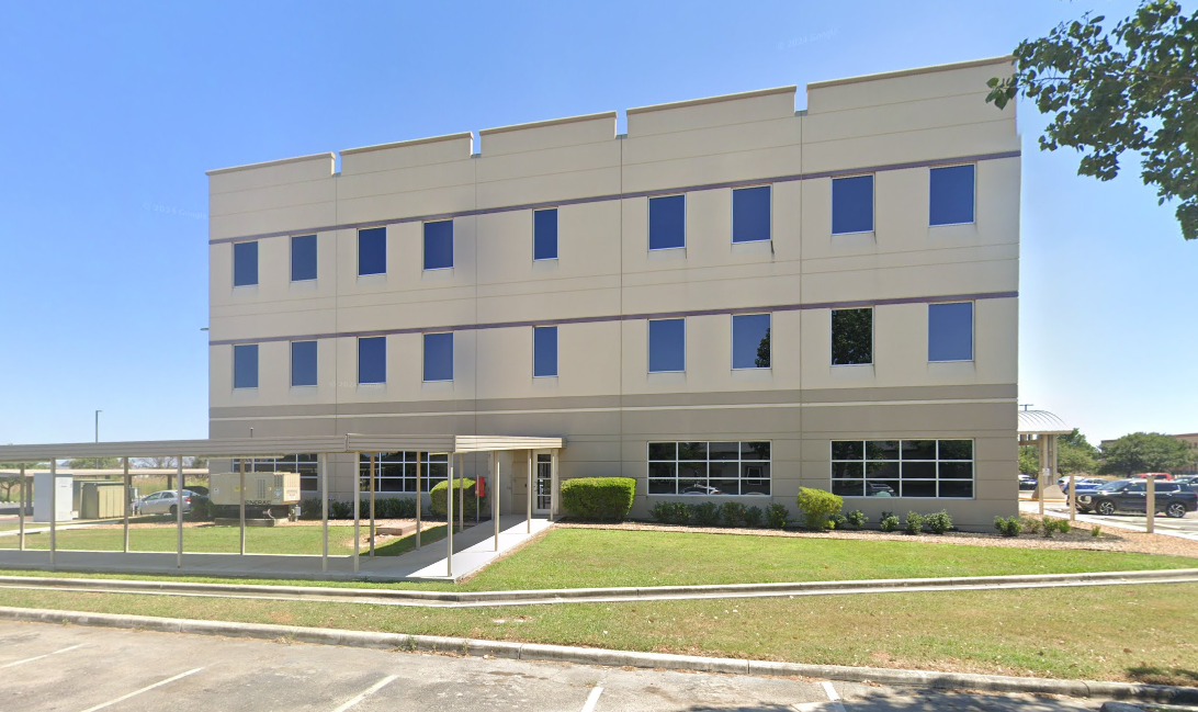 A large white building with a lot of windows is surrounded by trees and grass.