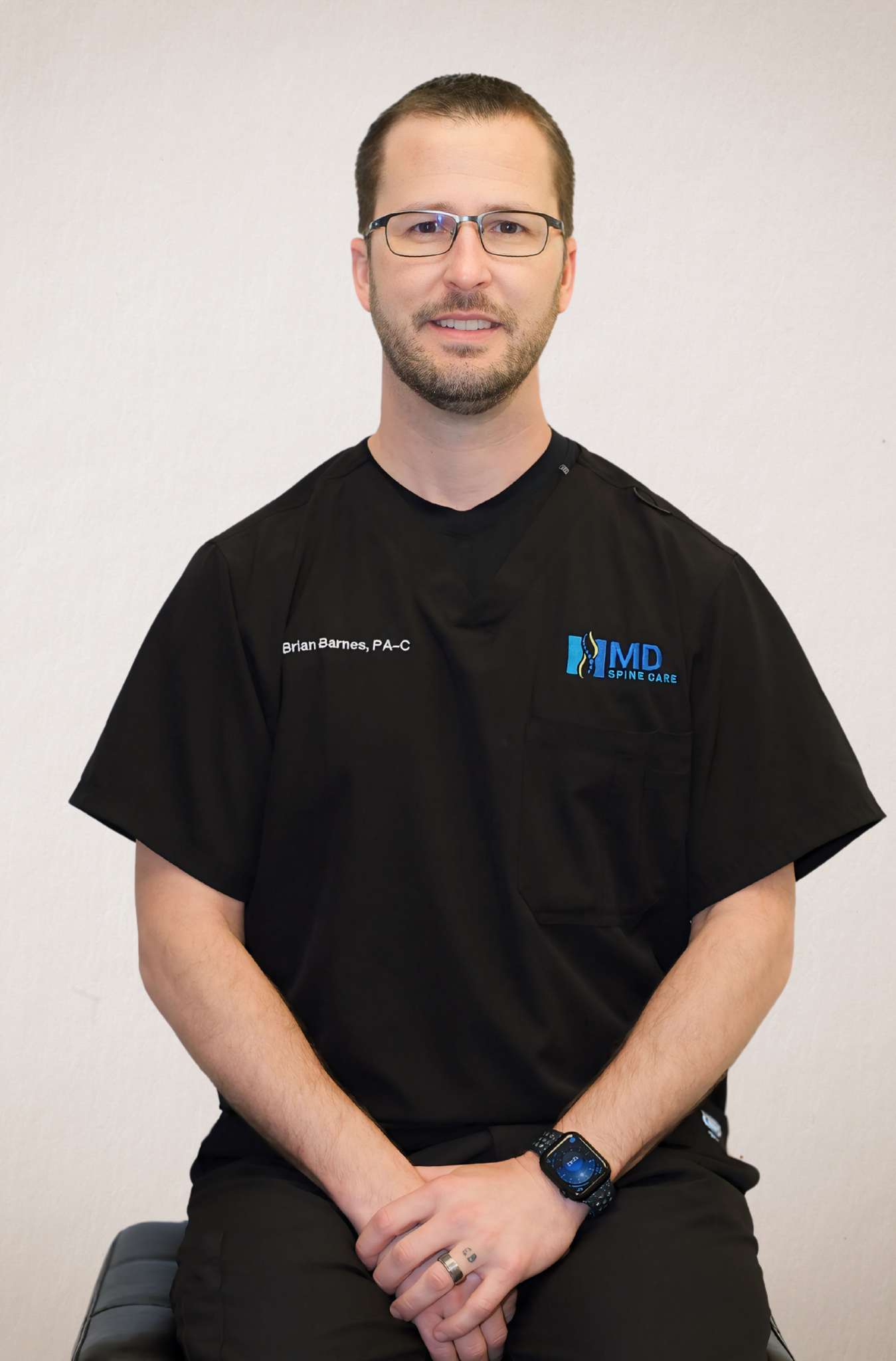 A man wearing a black scrub top with the word rwe on it