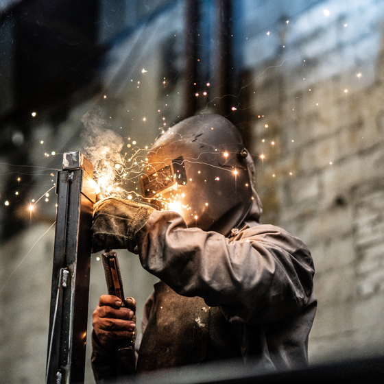 A man wearing a welding mask is welding a piece of metal