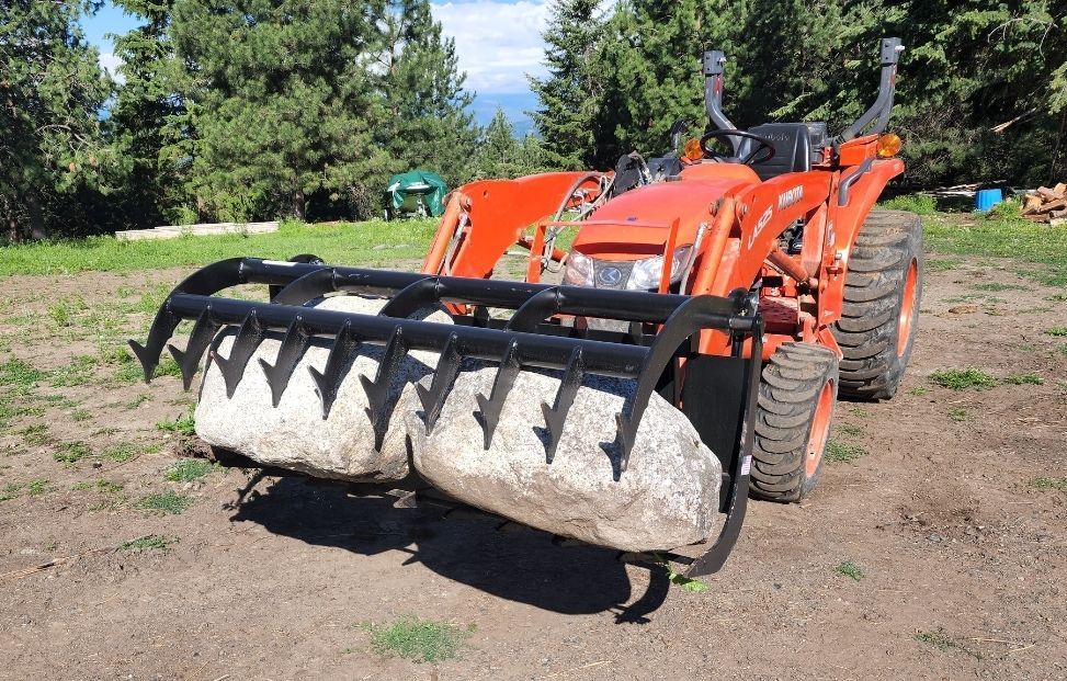 A tractor with a large rock attached to it is parked in a field.