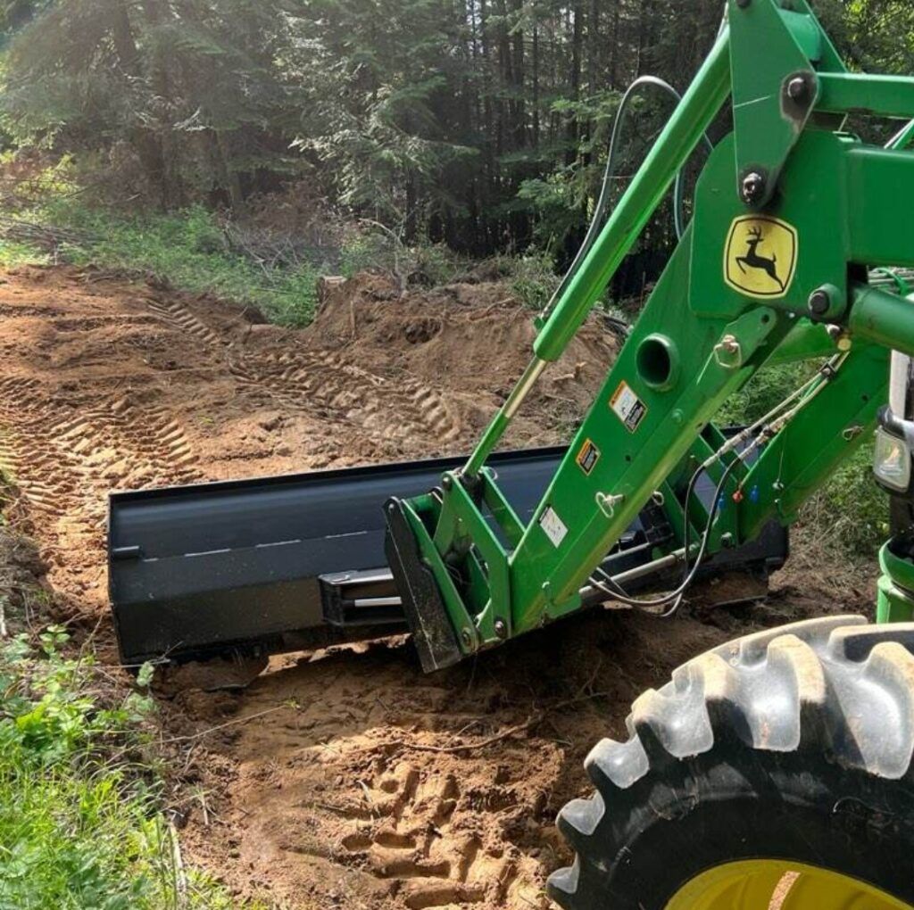 A green john deere tractor is moving dirt on a dirt road