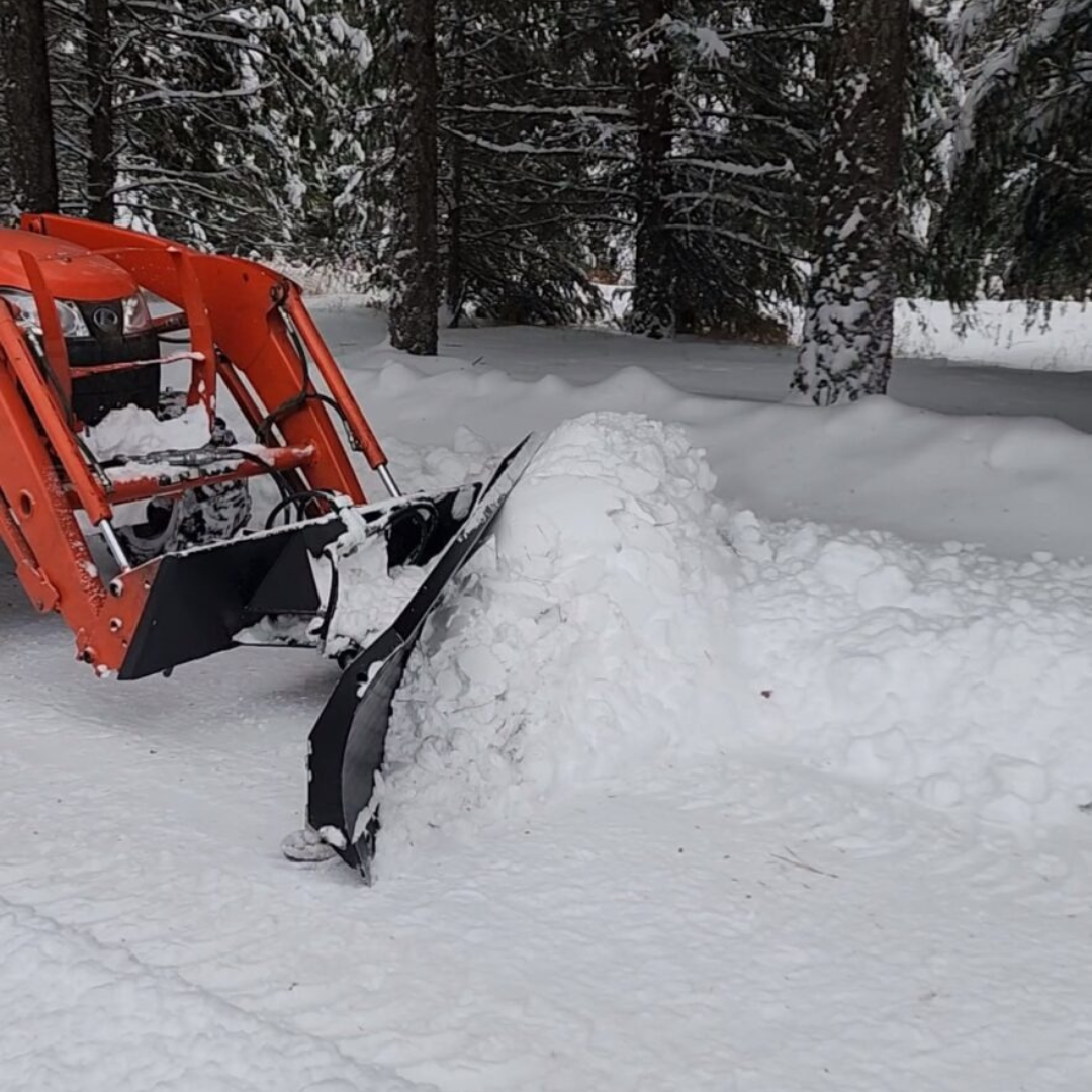 An orange snow plow is plowing a large pile of snow