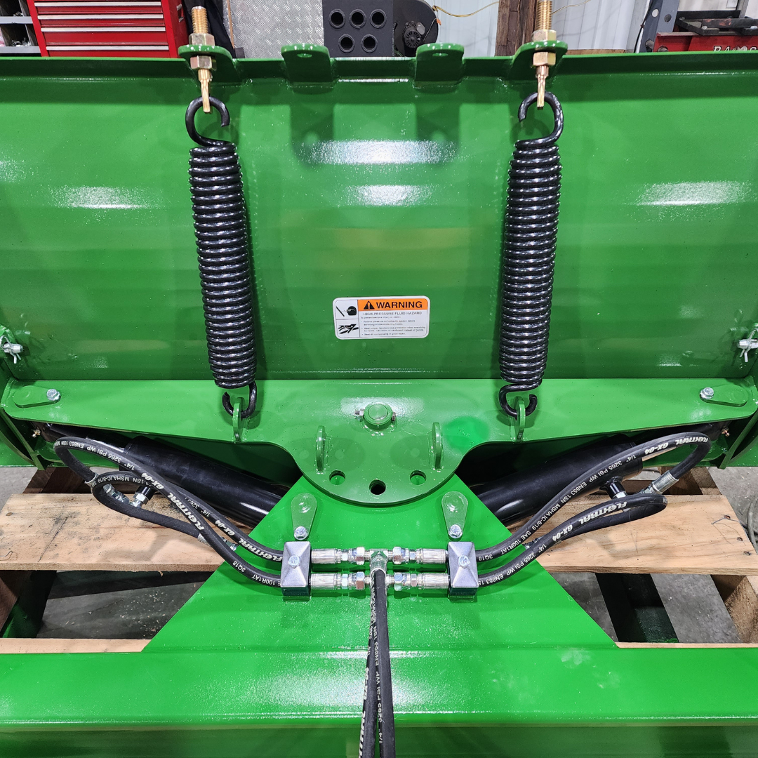 A green snow plow is sitting on top of a wooden pallet.