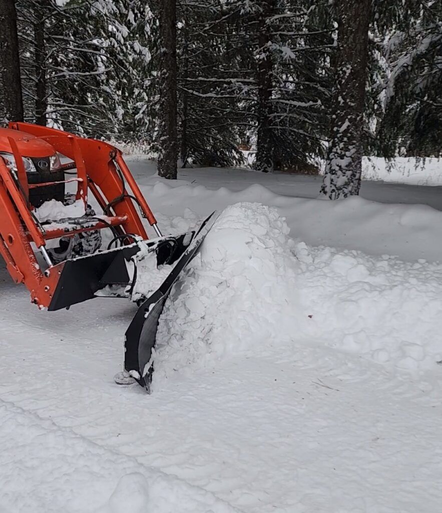 A snow plow is sitting in the middle of a snowy field.