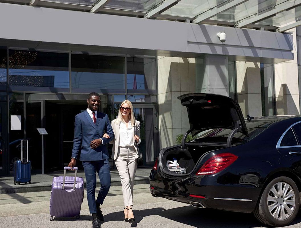 A man and a woman are walking towards a car with their luggage.