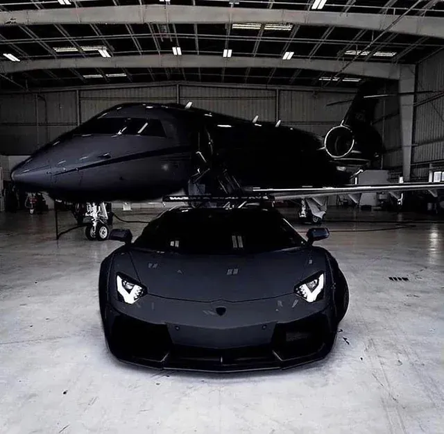A black car is parked next to a black plane in a hanger