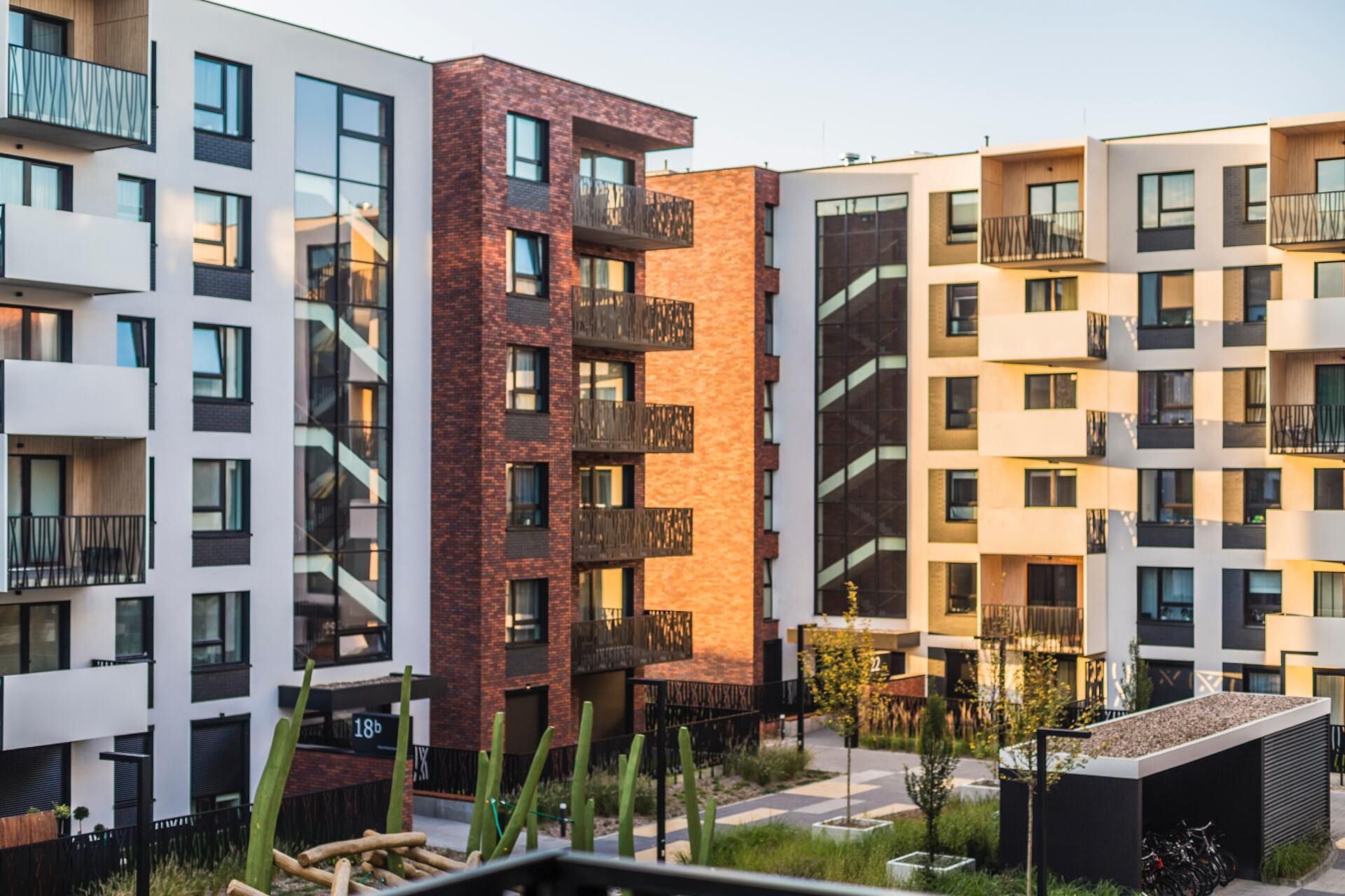 Modern apartment complex exterior with brick and white facades, balconies, and a courtyard.