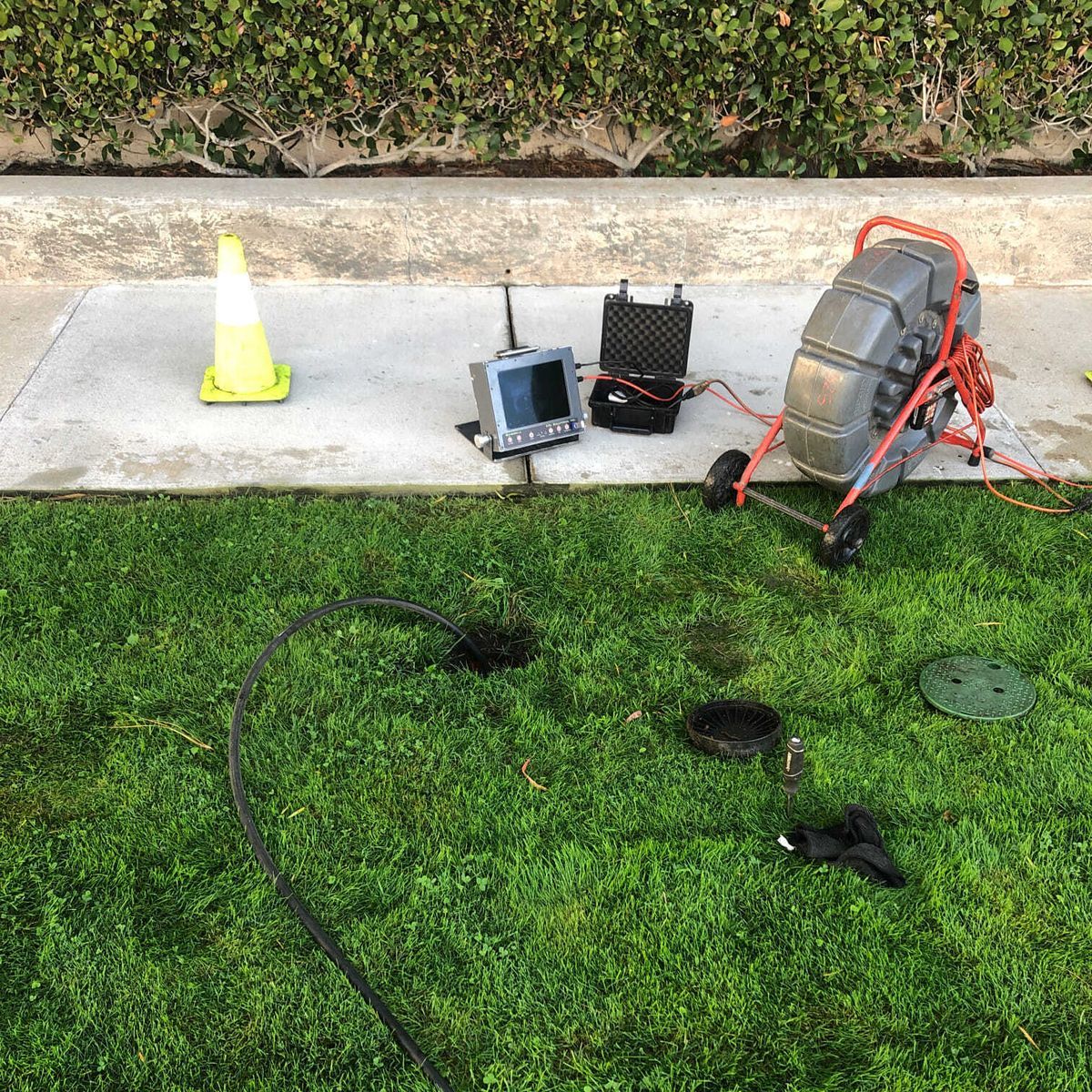 Plumbing inspection equipment on grass: camera, reel, monitor, and open manhole.