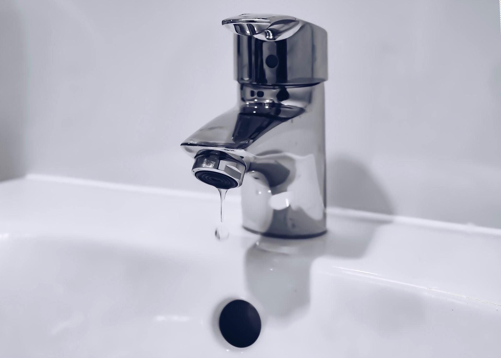 Chrome faucet drips water into a white sink.