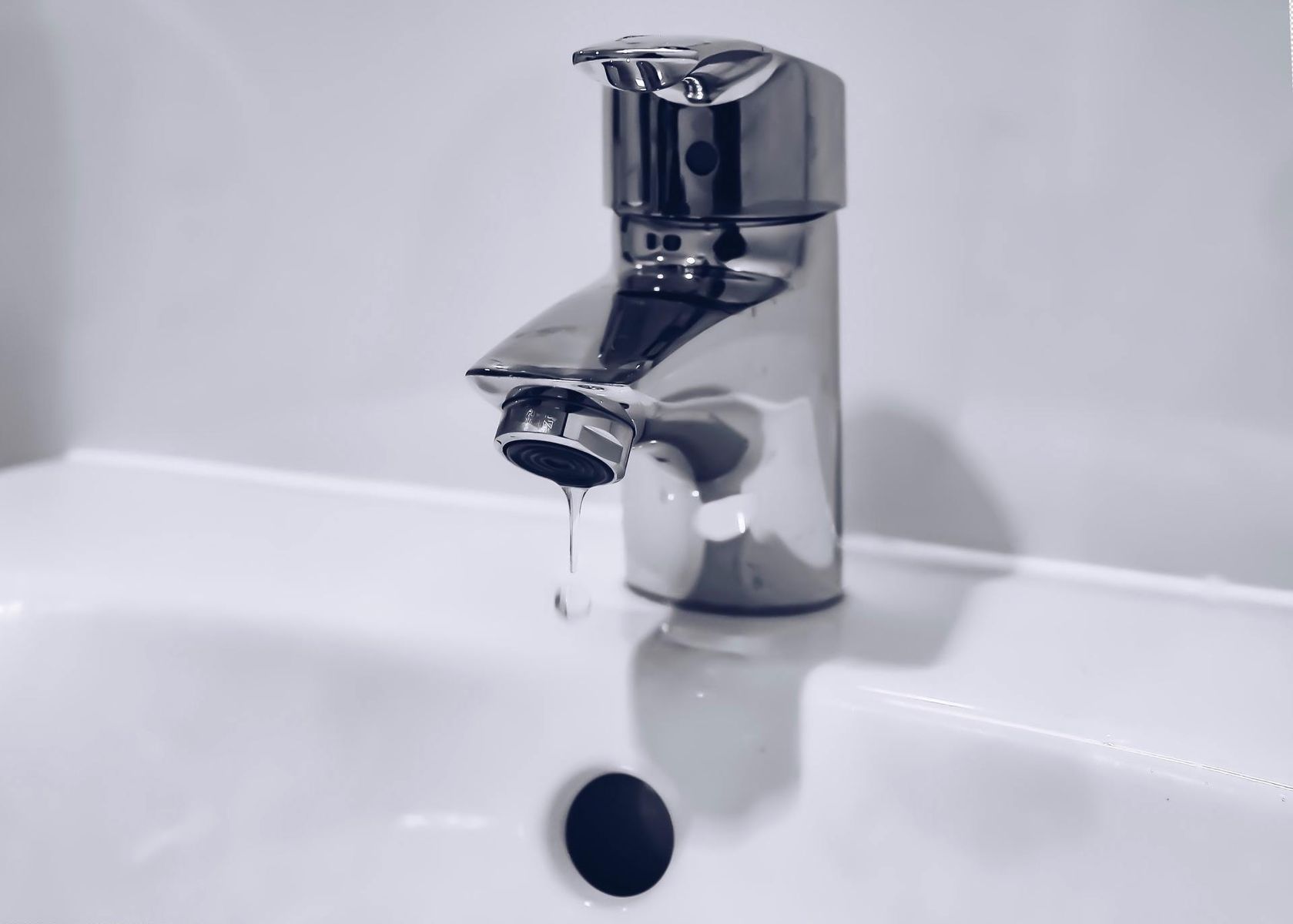 Chrome faucet dripping water into a white sink.