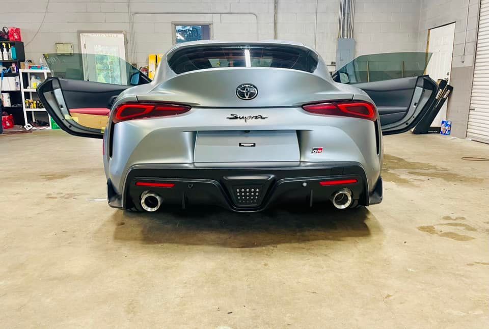Rear view of a silver Toyota Supra with doors open in a garage.