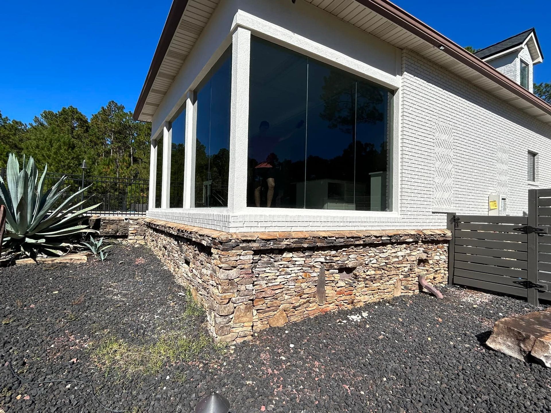 A modern house with floor-to-ceiling windows and stone facade against a clear blue sky.