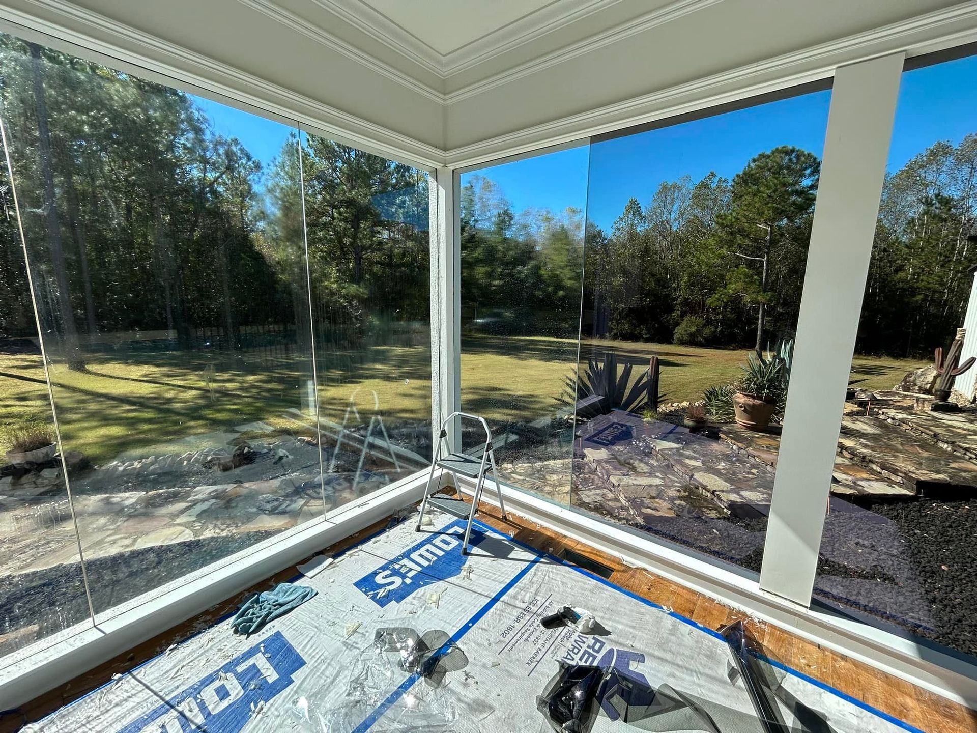 Sunroom with large glass windows overlooking a backyard. Construction materials visible on the floor.