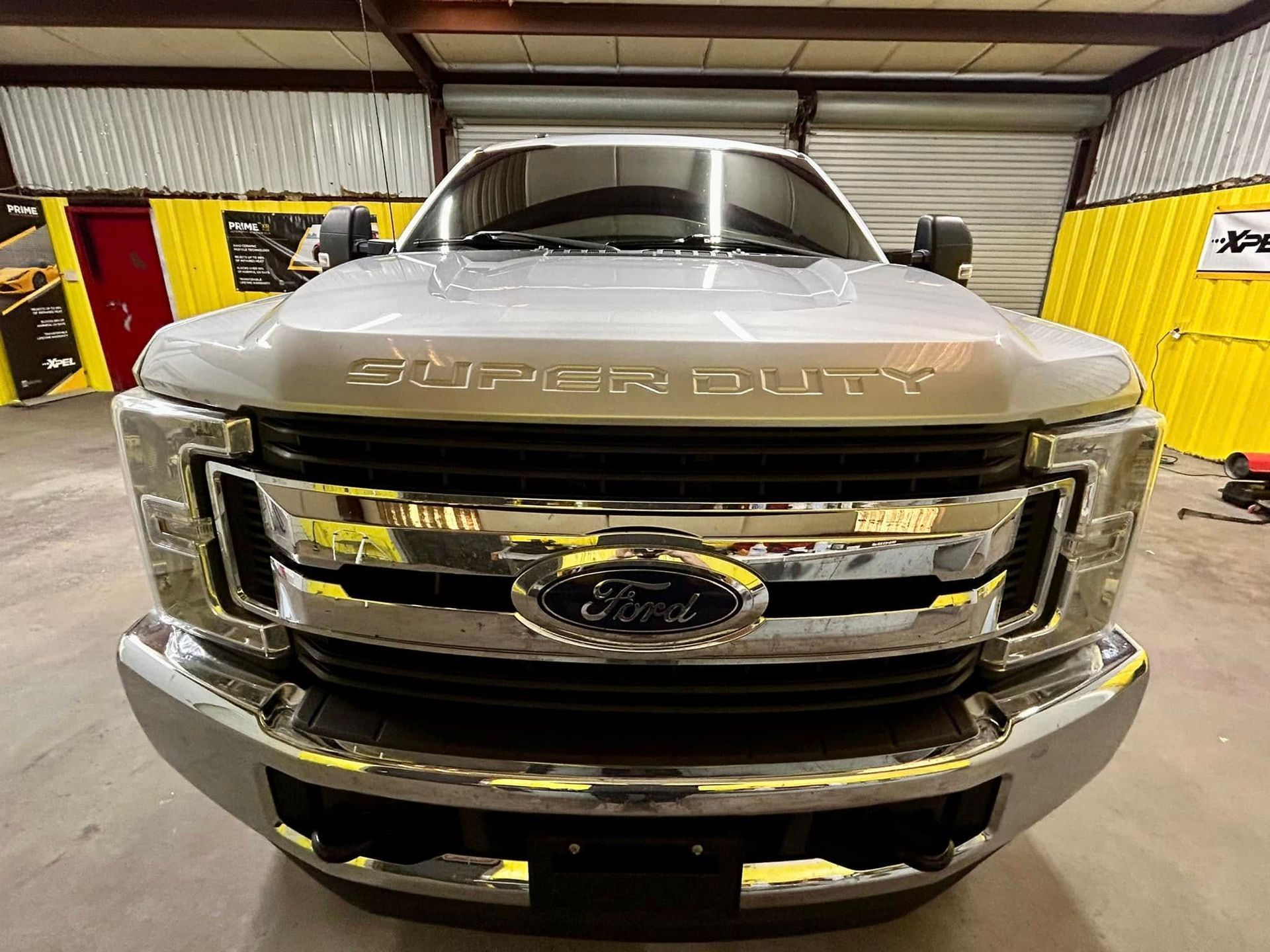 Silver Ford Super Duty truck, front view, chrome grill and bumper, indoor setting.
