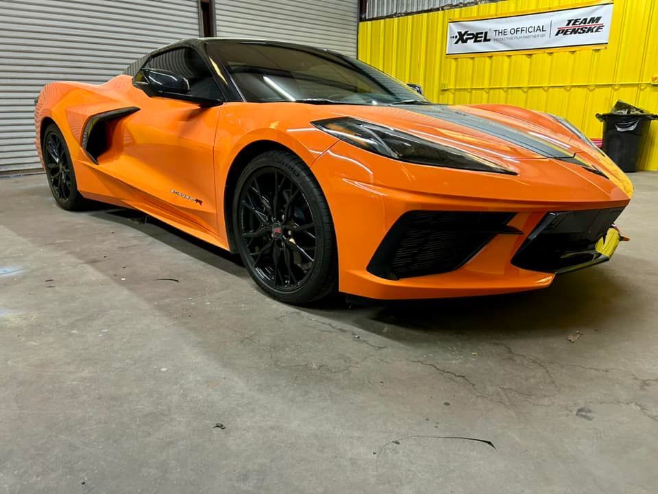Orange sports car with black wheels and a silver stripe, in a garage.