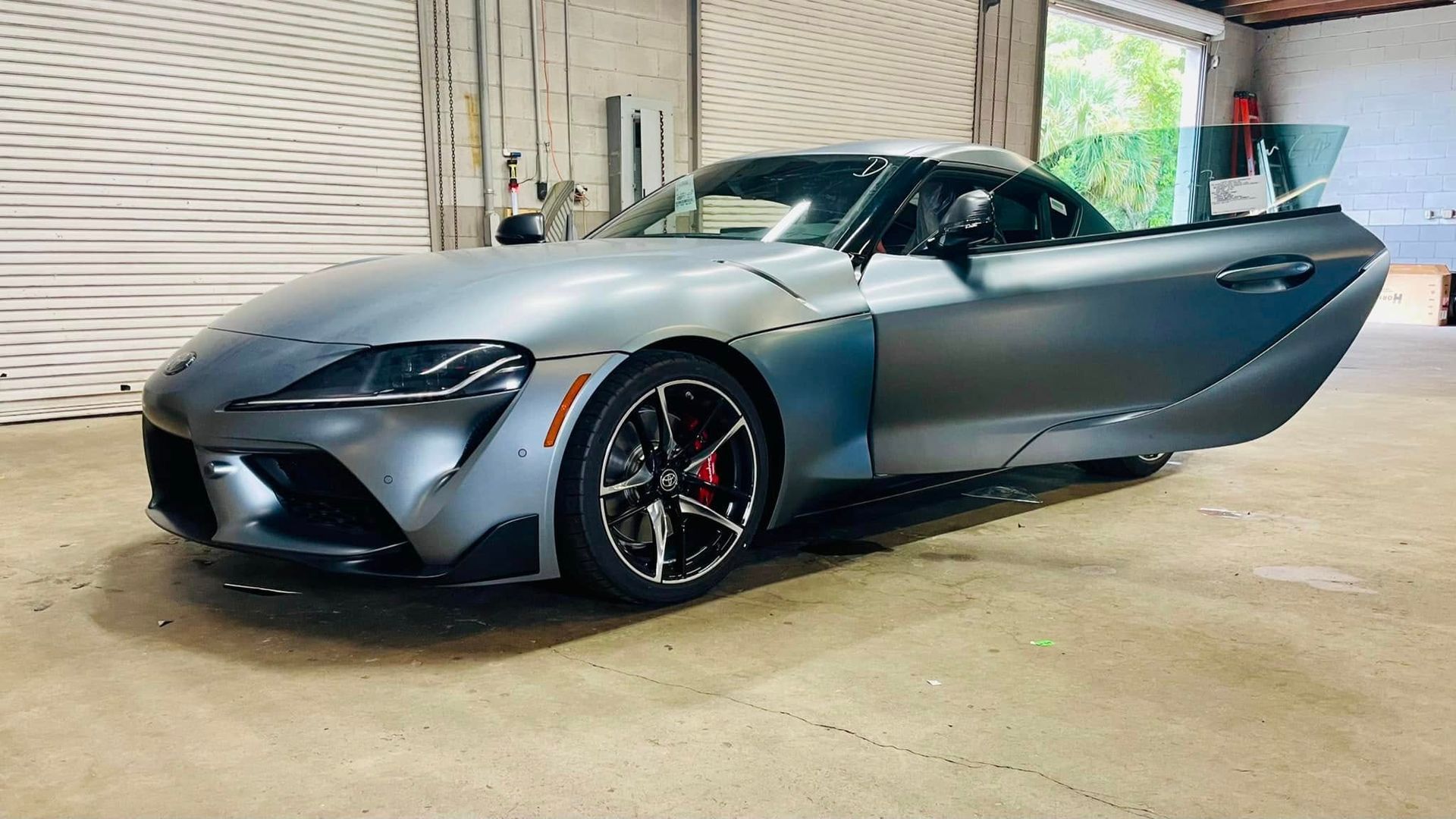 Gray Toyota Supra sports car with open door in garage.