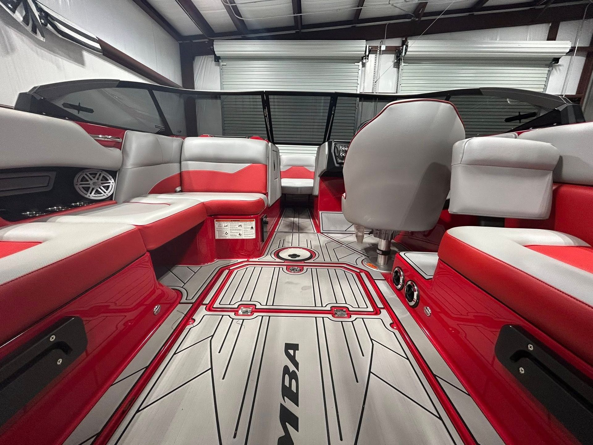 Interior of a boat with red, white, and gray seating and flooring. The boat is inside a building with a closed garage door.
